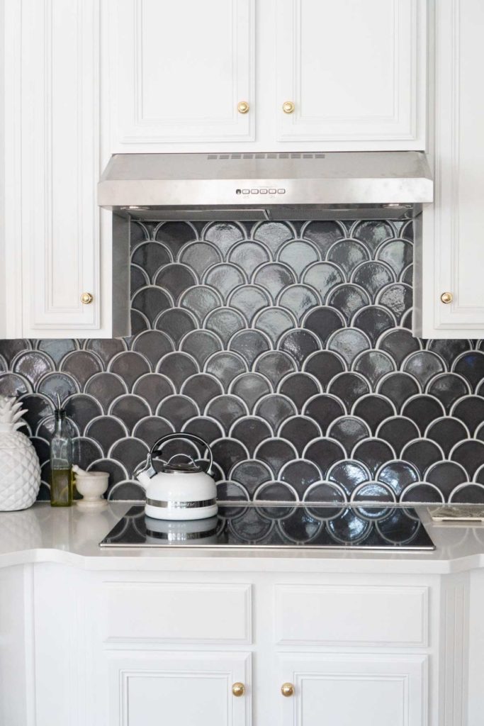 white kitchen cabinets with induction cooktop and blue fish scale tile backsplash