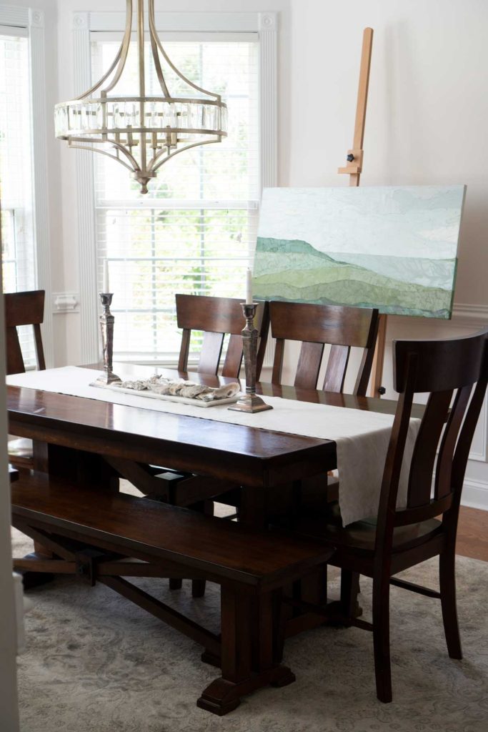 dining room table with chandelier and large painting on easel