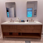 wood vanity with white counter and gold mirrors and fixtures
